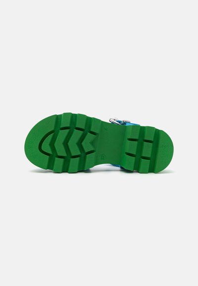 Sandală albastră cu o talpă groasă din cauciuc verde, prezentând un model în zigzag, cataramă ajustabilă și o suprafață texturată pentru aderență.