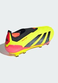 Chaussure de football jaune vif avec un dessus texturé noir et des accents roses. Présente une forme aérodynamique et plusieurs rayures noires sur le côté.