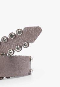 Pulsera de cuero en gris apagado con un acabado texturizado, que cuenta con tachuelas plateadas y piedras de strass a lo largo de los bordes. Detalle decorativo en la punta con forma puntiaguda.