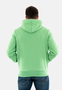 Felpa verde menta realizzata in tessuto morbido, con un ampio cappuccio regolabile, polsini e orlo a coste, abbinata a jeans blu.