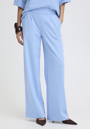 Femme portant un pantalon large taille haute bleu clair avec des plis, associé à des talons foncés à bout pointu et un haut assorti bleu clair.
