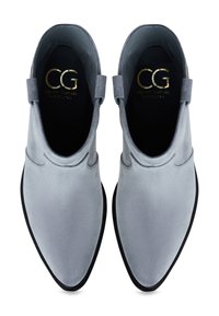 Botas de tobillo de ante gris con puntera puntiaguda, suela negra y una pequeña pestaña en el talón. Branding dorado visible en el interior.