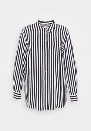 Chemise à manches longues rayée verticalement en noir et blanc avec un col et une fermeture à boutons sur toute la longueur, dotée de poignets rayés contrastés.