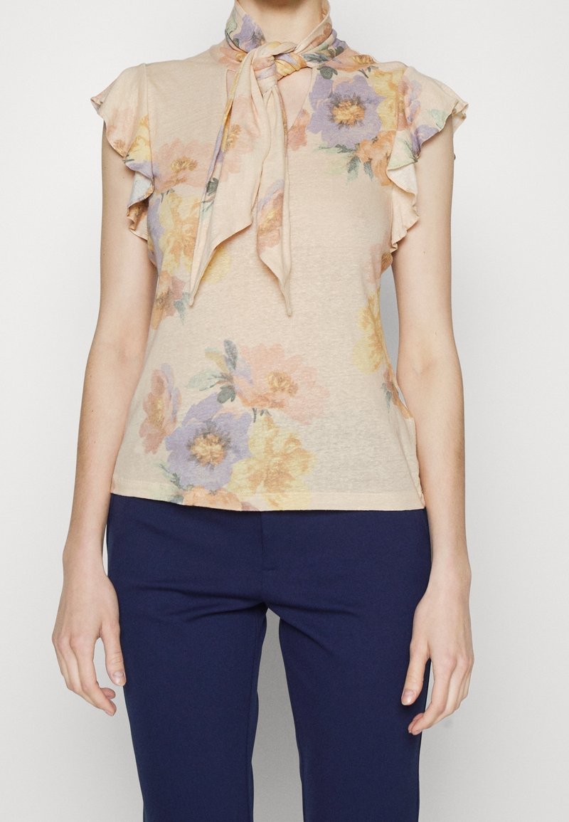 Beige blommig blus med korta volangärmar och en knutna scarf-halsringning, matchad med mörkblå åtsittande byxor.