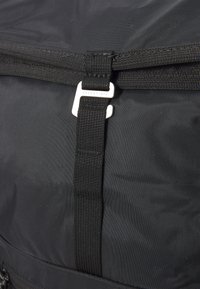 Schwarze Nylon-Tasche mit einem stabilen Reißverschluss, verstärkten Nähten und einem Metallclip für einen sicheren Verschluss. Strukturierte Oberfläche mit minimaler Detailgestaltung.