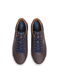 Barna szintetikus sportcipő tengerészkék fűzőkkel, fehér gumitalppal és világosbarna részletekkel a saroknál. Logó a nyelven.