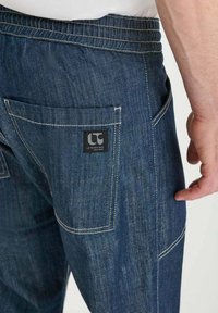 Donkerblauwe denim jeans met een licht taps toelopende snit. Kenmerken zijn een zwart labels en contrasterend wit stiksel op de zakken.