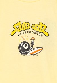 Geltona marškinėliai su juodu ir geltonu piešiniu, vaizduojančiu 8-balo personažą, laikantį picos gabalėlį ir banglentes. Tekstas skaito "Santa Cruz Skateboards."