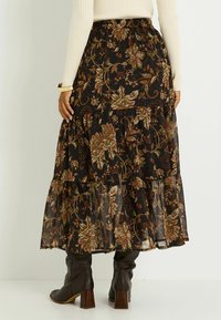 Jupe maxi noire à motifs floraux, avec des motifs verts et rouille. Tissu léger et fluide, associée à des bottes brunes à talons, montant jusqu'aux genoux.