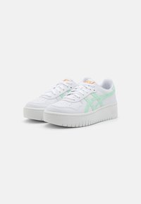 White sneakers with a textured leather upper, light mint green accents, and a chunky white outsole with ridged detailing. Orange logo on tongue.