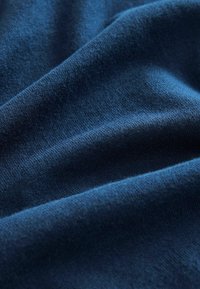 Weicher blauer Stoff mit glatter Textur, der sanfte Falten und eine leicht reflektierende Oberfläche aufweist und eine tiefblaue Farbe zeigt.