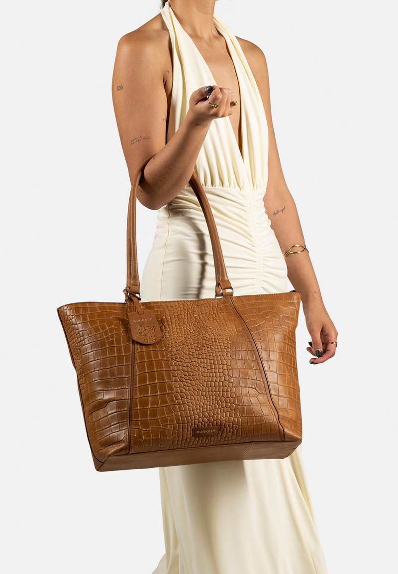 Sac fourre-tout en cuir synthétique crocodile marron avec deux anses, arborant une surface texturée et une étiquette de marque attachée.