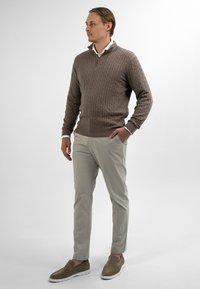Bruine kabelgebreide trui met een halve rits, lichtbeige chino's en taupe instapschoenen. Glad textuur en neutraal kleurenpalet.
