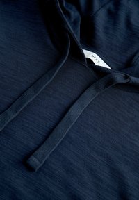 Gros plan sur le tissu d'un sweat à capuche bleu marine montrant des cordons texturés et une étiquette de vêtement blanche avec le texte "NEXT" à l'intérieur de la capuche.