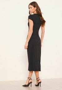 Fekete, testhez simuló midi ruha rövid ujjakkal, varrás nélküli kialakítással és sima textúrával. Fekete, pántos, magas sarkú cipővel párosítva.