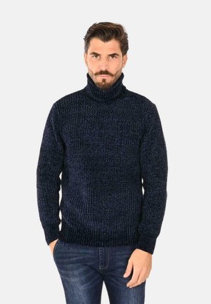 Maglione a collo alto navy realizzato in tessuto a maglia testurizzata, con polsini e orlo a coste, indossato con jeans in denim su uno sfondo semplice.