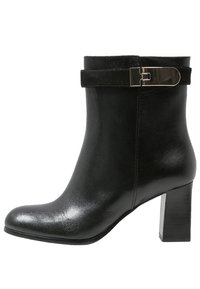 Bota de cuero negro para el tobillo con acabado brillante, con una correa de ante y detalle de hebilla metálica, y un tacón alto y grueso.