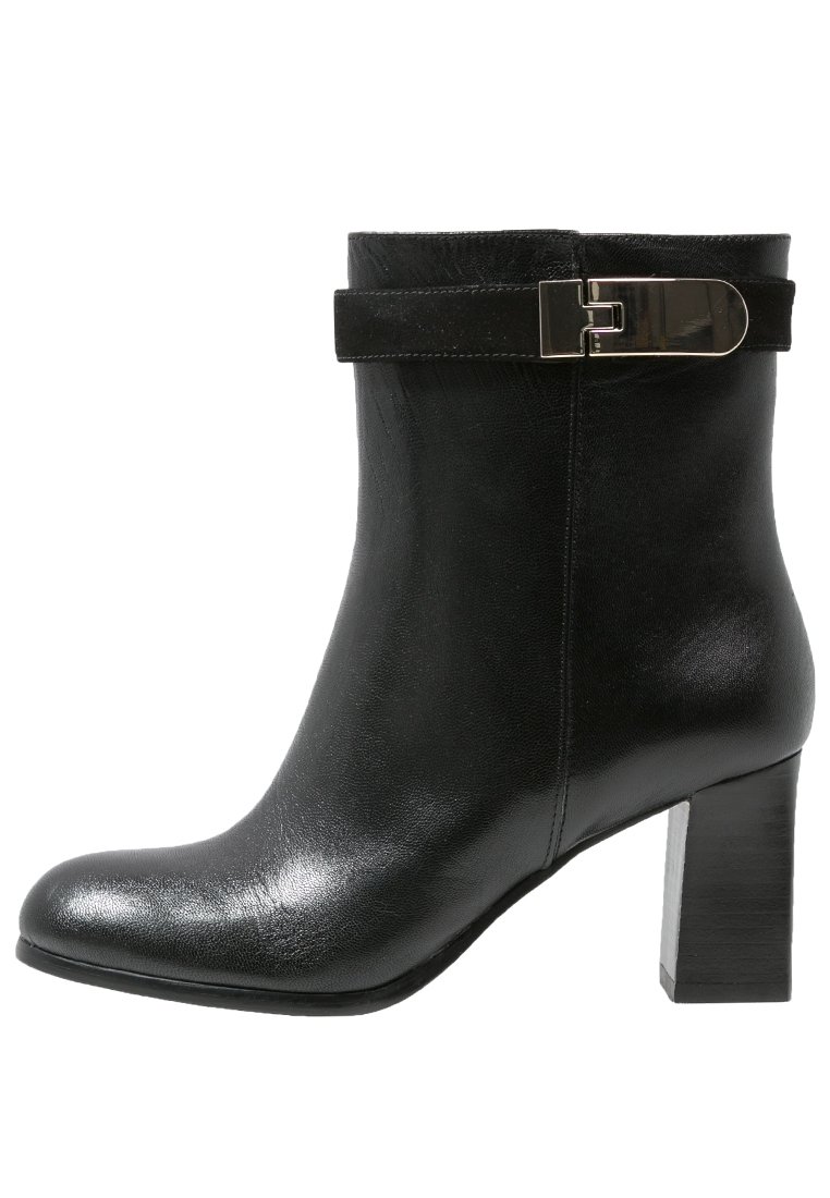 Bota de cuero negro para el tobillo con acabado brillante, con una correa de ante y detalle de hebilla metálica, y un tacón alto y grueso.