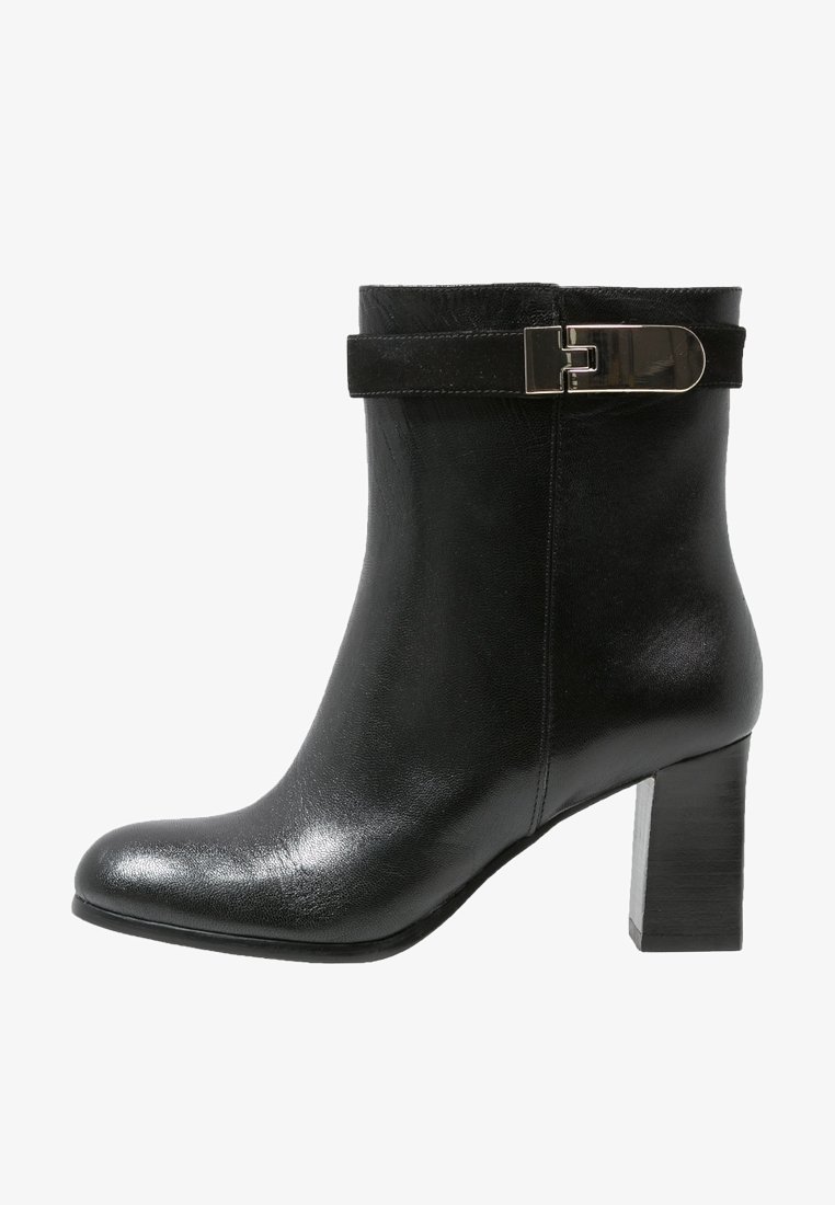 Bota de cuero negro para el tobillo con acabado brillante, con una correa de ante y detalle de hebilla metálica, y un tacón alto y grueso.