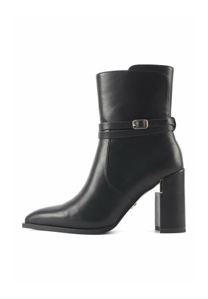 Black leather ankle boot with a pointed toe, mid-height block heel, and a decorative strap featuring a gold-tone buckle detail.