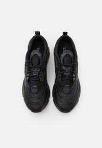 Svarta sportskor med ett mönstrat meshupp, rund tå och snörningsdesign. Har en tjock sula och dragflik vid hälen för enkel påtagning.