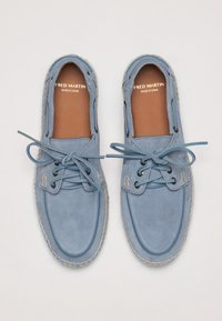 Chaussures en suède bleu clair avec un bout rond, un design à lacets et des coutures contrastantes. Semelle intérieure brun clair portant l'inscription "FRED MARTIN FABRIQUÉ EN ESPAGNE."