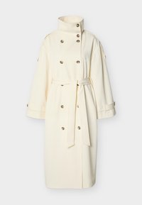 Εκρού μακρύ παλτό τρεντς με ψηλή γιακά, διπλό κούμπωμα με κουμπιά, φαρδιές μανσέτες και ζώνη δεμένη στη μέση.