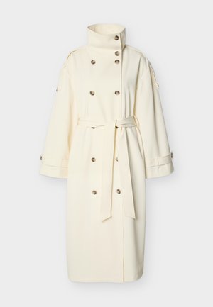 Εκρού μακρύ παλτό τρεντς με ψηλή γιακά, διπλό κούμπωμα με κουμπιά, φαρδιές μανσέτες και ζώνη δεμένη στη μέση.