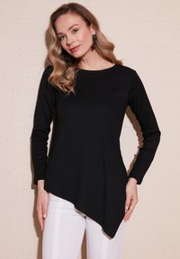 Maglietta nera a maniche lunghe con orlo asimmetrico anteriore, texture a coste e scollatura rotonda, abbinata a pantaloni bianchi.