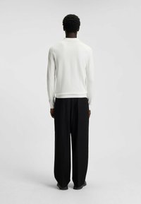 Maglione bianco con maniche lunghe e orlo a coste, abbinato a pantaloni neri larghi. Il tessuto sembra liscio con un design minimalista.