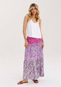 Bílý bezrukávový top spárovaný s dlouhou, vícebarevnou maxi sukní s růžovými a modrými paisley vzory a horizontálními pruhy. Hnědé sandály.