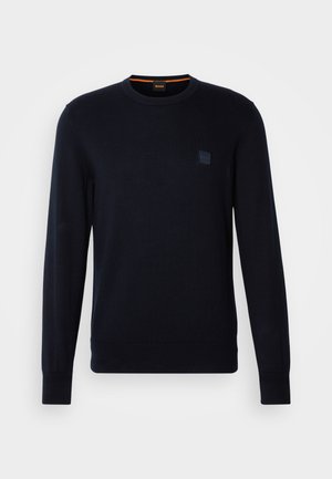 Navy blue knit sweater with long sleeves, crew neckline, ribbed cuffs and hem, featuring a small square logo patch on the chest.