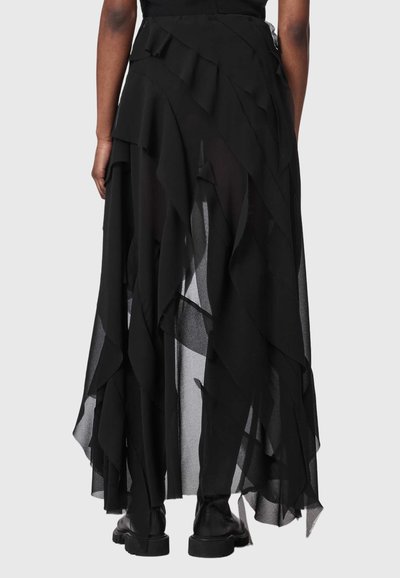 Personne portant une jupe noire transparente à plusieurs couches avec un ourlet asymétrique et des bottes noires épaisses, vue de dos sur un fond uni.