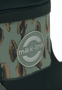 Zaļi ūdensizturīgi zābaki ar teksturētu melnu gumijas zoli, militāra stila rakstu un sudraba apļa logotipu, iepresētu sānos.