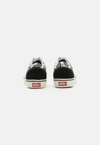 Black and white canvas sneakers with a bandana pattern, featuring black suede accents, white laces, and a red logo on the sole.
