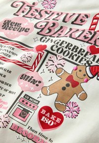 White fabric featuring colorful text and graphics for baking gingerbread cookies. Includes a gingerbread man, snowflakes, and a recipe layout.