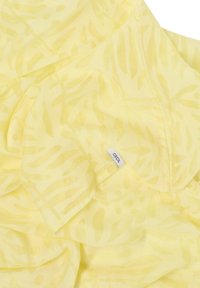 Tissu jaune avec un motif de feuilles, texture légère, et une petite étiquette portant l'inscription « CECIL » visible dans le coin.