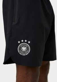 Μαύρα αθλητικά σορτς με ευθύ κοψίμα, που διακρίνονται για την ομαλή υφή τους. Κουβαλούν ένα εξέχον λευκό έμβλημα και τέσσερα αστέρια στο κάτω μέρος του ποδιού.