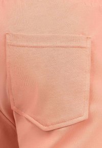 Tessuto in cotone pesca con una tasca quadrata e cuciture dritte sui bordi, che mostra una consistenza morbida e un colore uniforme.