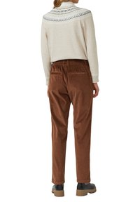 Jasnobeżowy sweter z ozdobnymi, czarnymi dzianinowymi detalami przy kołnierzu, w połączeniu z brązowymi, sztruksowymi spodniami z wysokim stanem, wyposażonymi w elastyczną talię i kieszenie.