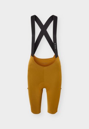 Culote corto de ciclismo en amarillo mostaza con tirantes cruzados negros en los hombros, zona de asiento acolchada y diseño hasta la rodilla.