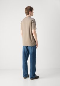 Beige bomull t-skjorte med korte ermer, rund hals, kombinert med løstsittende blå denimjeans og mørke sko. Sett bakfra.