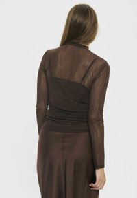 Maglietta marrone trasparente a maniche lunghe con un design texture. Tessuto arricciato e sottoveste visibile. Gonna marrone liscia e fluida sottostante.