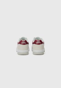 Bijele tenisice s laganom sivom antilop kožom i crvenim kožnim potpeticama, s "New Balance" logotipom. Glatka tekstura i umjereni ulošci, klasični dizajn.