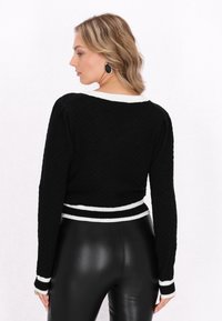 Schwarzer strukturierter Pullover mit weißen gestreiften Bündchen und Saum, mit langen Ärmeln und rundem Ausschnitt, von hinten gezeigt.