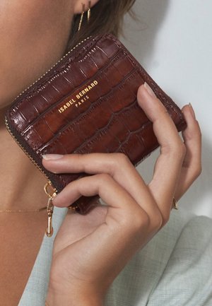 Bruine krokodillenembossed leren portemonnee met gouden hardware en rits. Voorzien van de merknaam "ISABEL BERNARD PARIS" geprint op de voorkant.