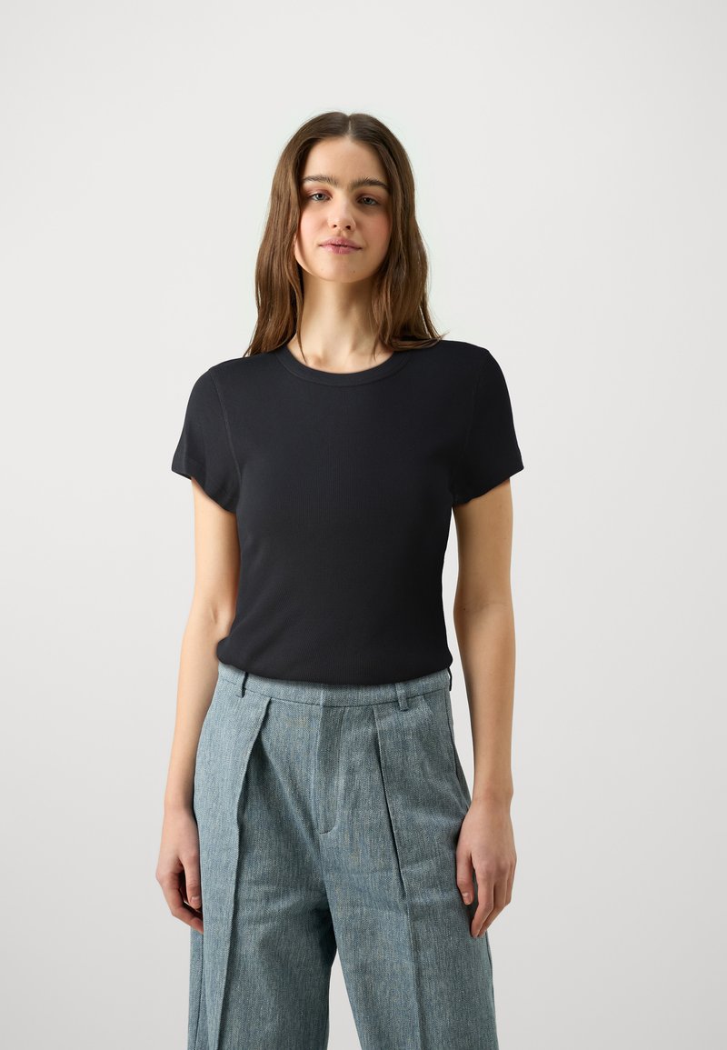 T-shirt nero a maniche corte con scollatura rotonda e design aderente, abbinato a pantaloni plissettati azzurri. Texture liscia e minimalismo nei dettagli.
