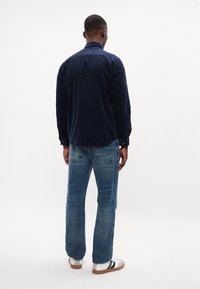 Marineblå kordfløjls skjorte med knapmanchetter, parret med lyseblå straight-leg denim jeans og hvide sneakers med sorte accenter.