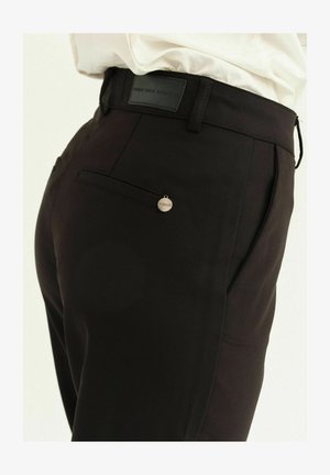 Sorte skræddersyede bukser med en glat tekstur, som har en baglomme og en lille cirkulær metalaccent med teksten "FISEAK."