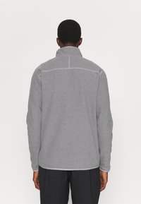 Chaqueta de felpa gris con un cuello alto, costuras planas y dobladillo recto. Presenta una textura sólida y sin patrones visibles.